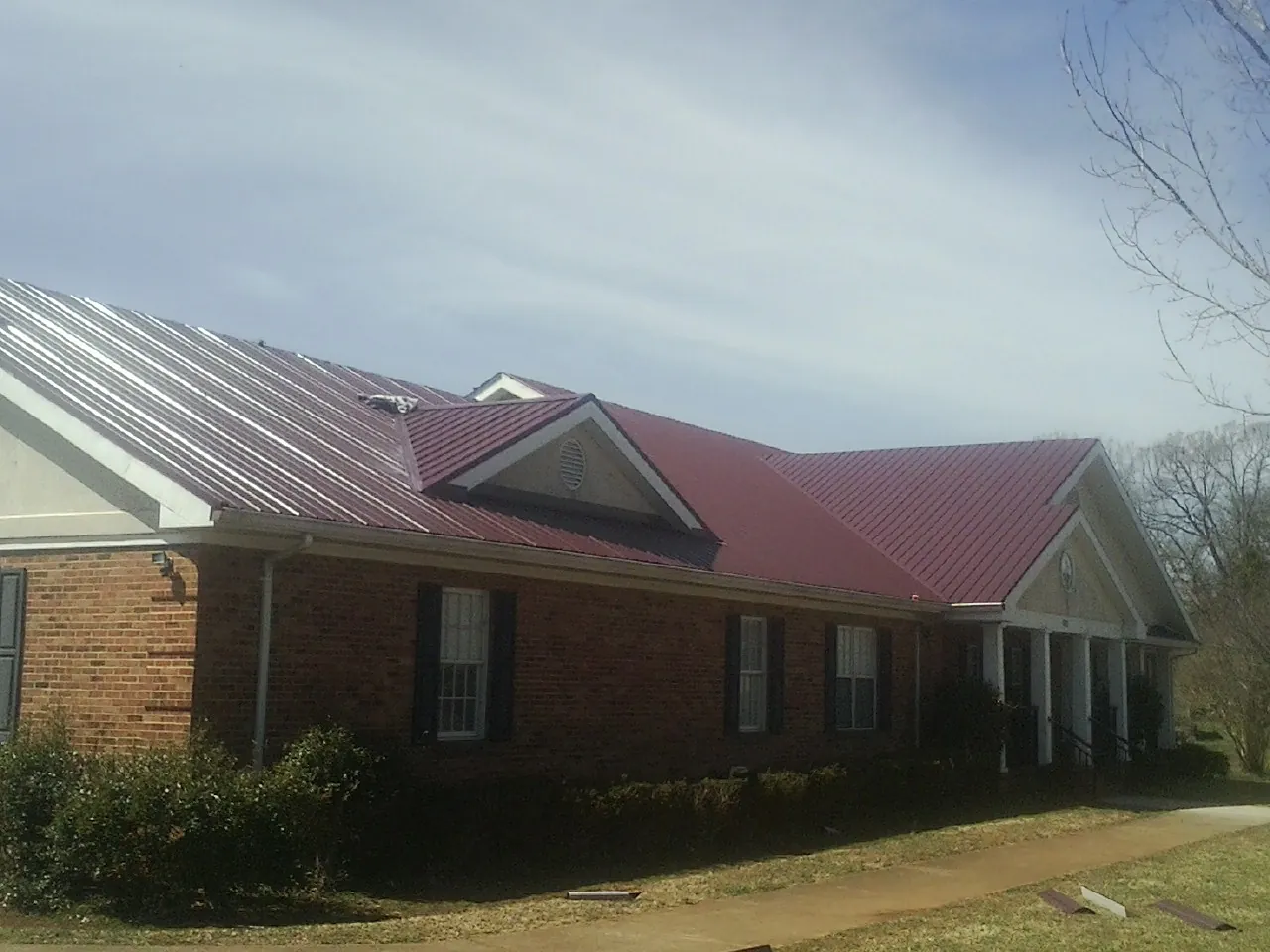 Red metal roof with gabled entries on a long brick building, from a Hail Damage Roof Repair job in St Columbans