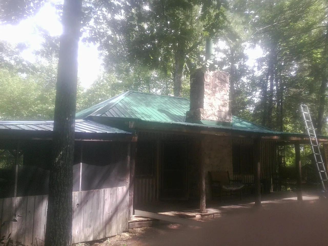 Green metal roof and stone chimney above a log cabin porch in St Columbans