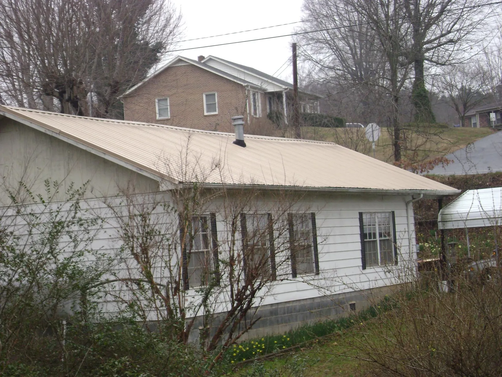 Tan metal roof on a white sided house set into a hillside — Commercial Roofing by Roofing Brothers in St Columbans